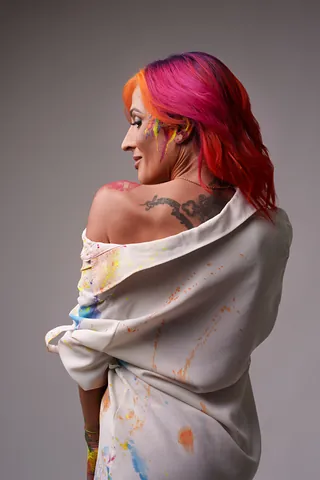 Isa de espaldas, con la cara de perfil y la camisa salpicada de pintura cayendo por los hombros